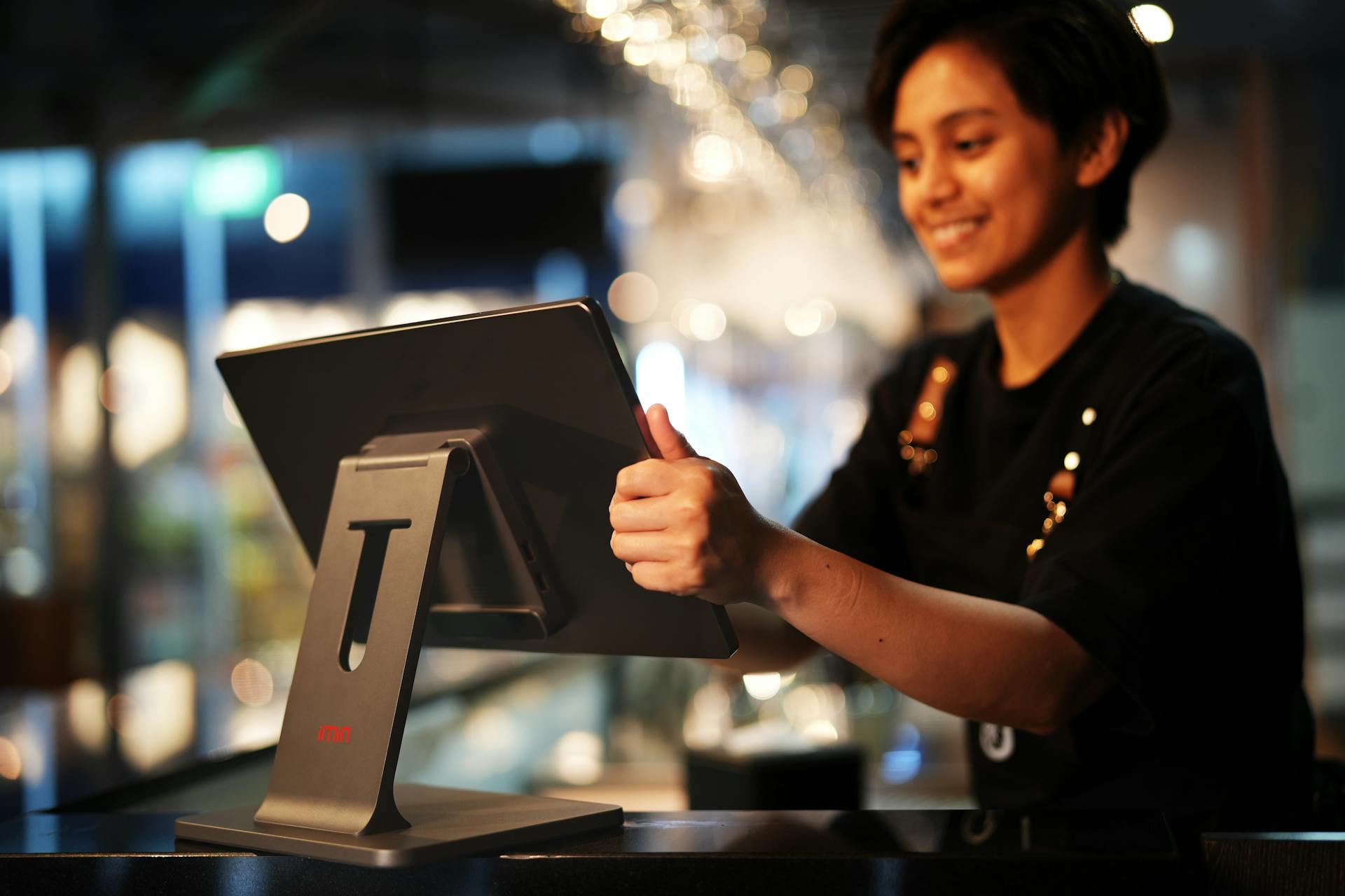A person wearing a black shirt operates a touchscreen register 
            at a counter in a brightly lit indoor setting.